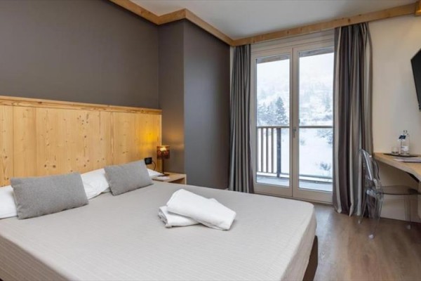 Nowocześnie urządzony pokój hotelowy z podwójnym łóżkiem i widokiem na ośnieżony krajobraz.