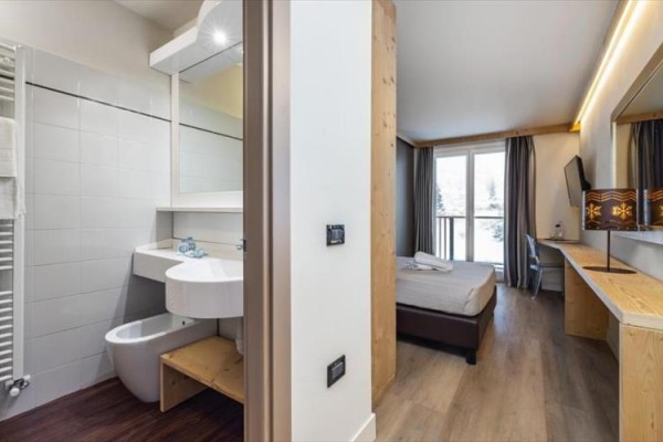 Nowoczesny pokój hotelowy z przylegającą łazienką, biurkiem i widokiem z balkonu.
