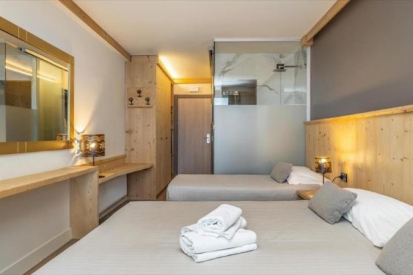 Dwa łóżka w nowoczesnym pokoju hotelowym z drewnianą boazerią i złożonymi ręcznikami.
