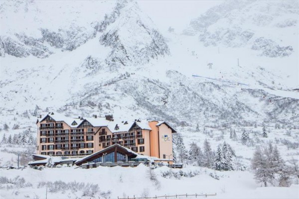 Hotel otoczony ośnieżonymi górami i drzewami w zimowej scenerii.