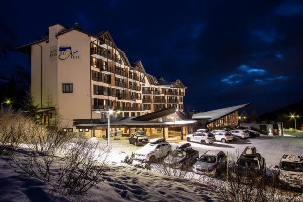 Hotel z oświetlonym parkingiem w zimowym krajobrazie o zmierzchu.