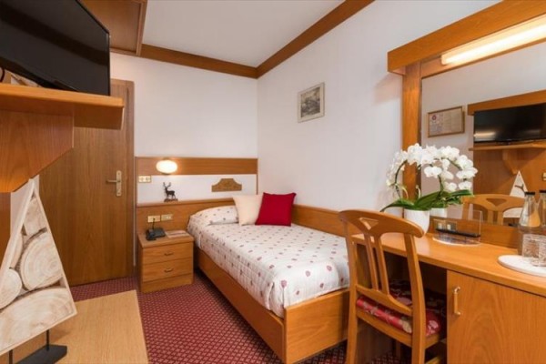 Jednoosobowy pokój hotelowy z drewnianymi meblami i białymi storczykami na stole.