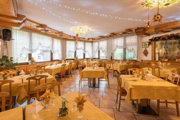 Restauracja z drewnianymi stołami i krzesłami, żółte obrusy oraz kwiatowa dekoracja na ścianach pod oknami.
