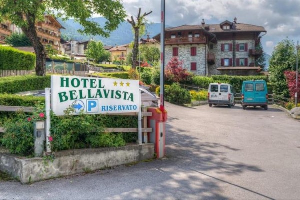 Hotel Bellavista obok parkingu z dwoma samochodami, otoczony zielenią.