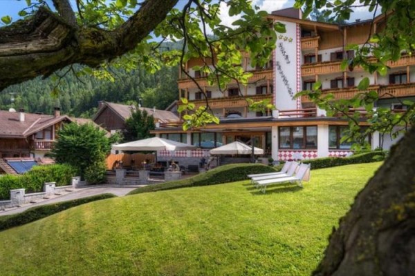 Hotel otoczony zielenią z leżakami na trawniku i drzewem na pierwszym planie.