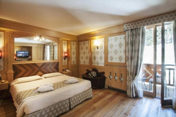 Pokój hotelowy z łóżkiem małżeńskim, drewnianą okładziną i balkonem.