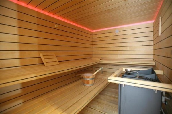 Drewniana sauna z ławką i piecem, podświetlona czerwonymi LEDami.