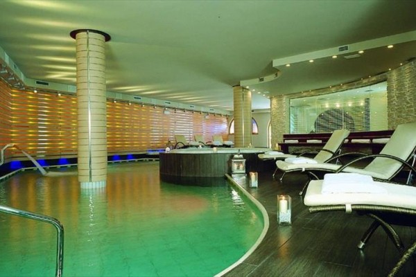 Luksusowe wnętrze spa z basenem, leżakami i świecami.