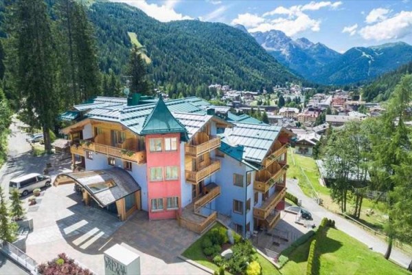 Hotel otoczony górami i lasami w słoneczny dzień.