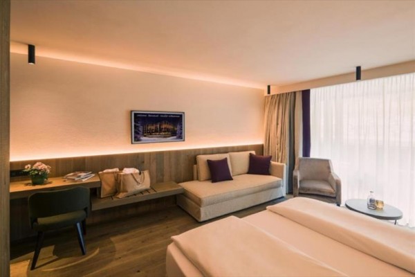Nowocześnie urządzony pokój hotelowy z dużymi oknami, łóżkiem, sofą i biurkiem.