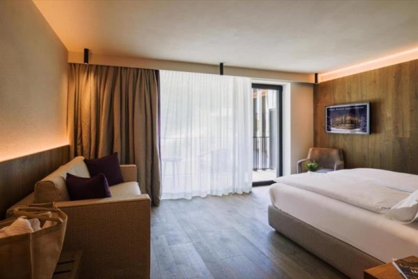 Nowocześnie urządzony pokój hotelowy z podwójnym łóżkiem, sofą i dużymi oknami.