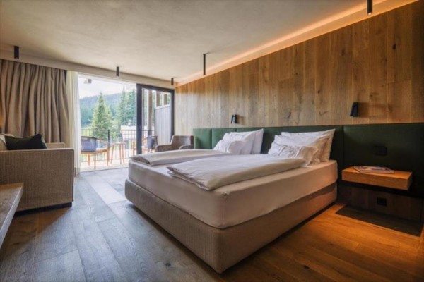 Nowoczesny pokój hotelowy z łóżkiem małżeńskim i balkonem z widokiem na drzewa.