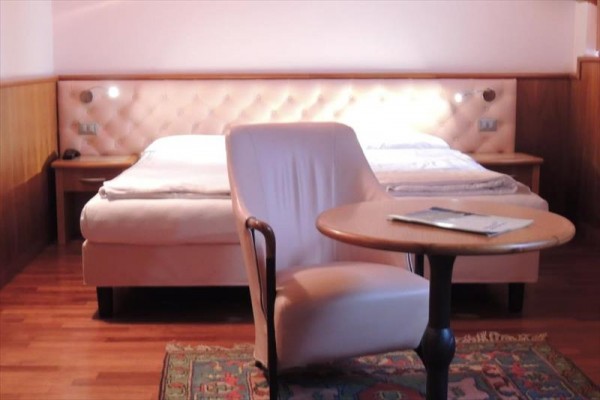 Pokój hotelowy z łóżkiem małżeńskim, fotelem i stołem.