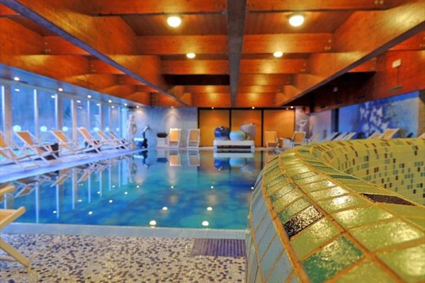 Pokój hotelowy z łóżkiem małżeńskim, fotelem i stołem.