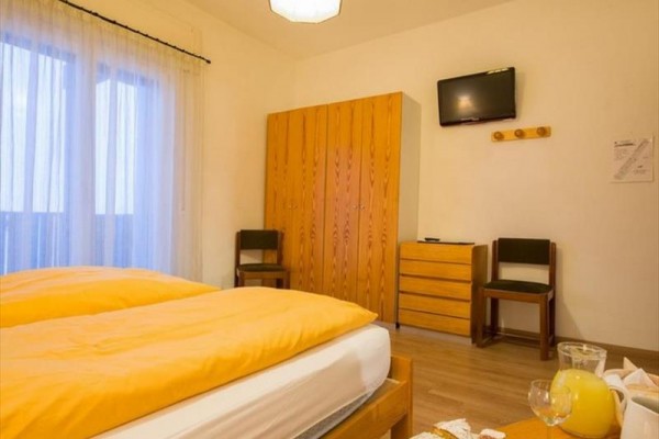 Pokój hotelowy z podwójnym łóżkiem, szafą, telewizorem i śniadaniem na stole.