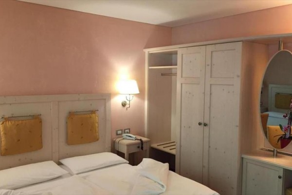 Pokój hotelowy z łóżkiem, szafą, lustrem i lampą na różowej ścianie.