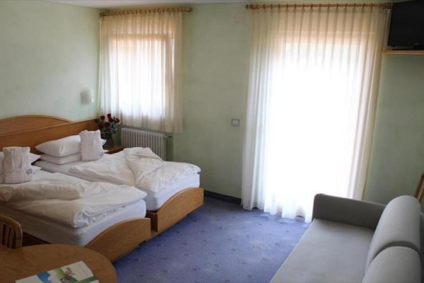 Jasny pokój hotelowy z dwoma łóżkami, sofą i oknem z białymi zasłonami.