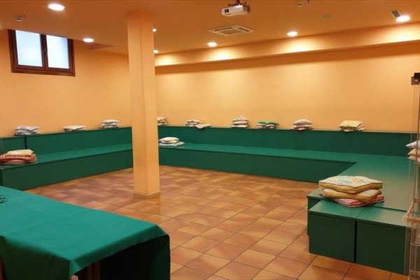 Pusta sala z ochrowymi ścianami, zielonymi ławkami i poduszkami.