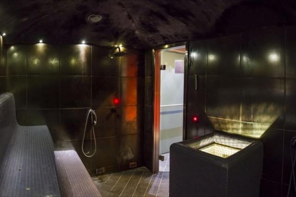 Nowoczesna sauna parowa z ławką, oświetleniem i drzwiami do innego pomieszczenia.