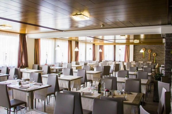 Restauracja z nowoczesnym wnętrzem i uporządkowanymi stołami z białymi obrusami.