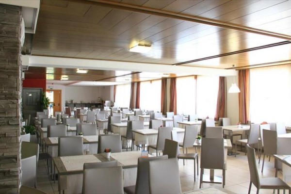 Przestronna restauracja z wieloma stolikami i szarymi krzesłami.