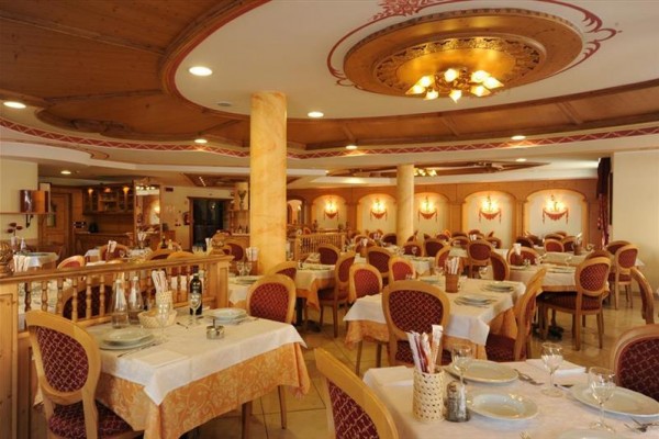 Wnętrze przestronnej restauracji z drewnianymi elementami i czerwonymi krzesłami przy stołach z białymi obrusami.