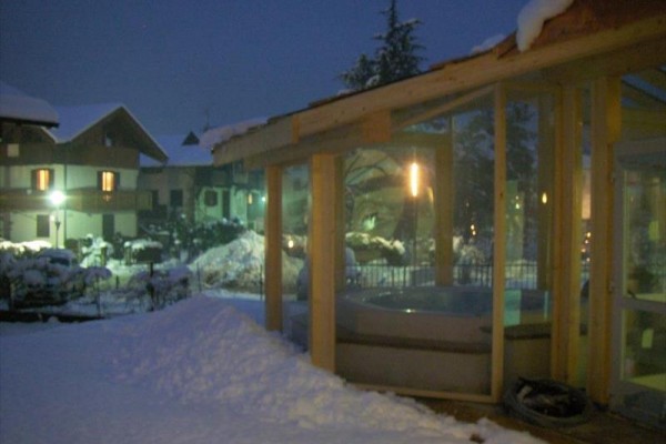 Taras pokryty śniegiem z widokiem na jacuzzi przez szklane ściany przy wieczornym oświetleniu.