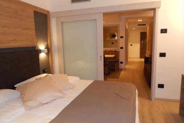 Nowoczesny pokój hotelowy z łóżkiem i przesuwnymi drzwiami prowadzącymi do aneksu kuchennego.