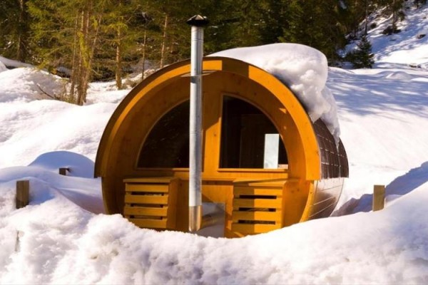 Drewniana sauna w kształcie beczki otoczona śniegiem w lesnym otoczeniu.