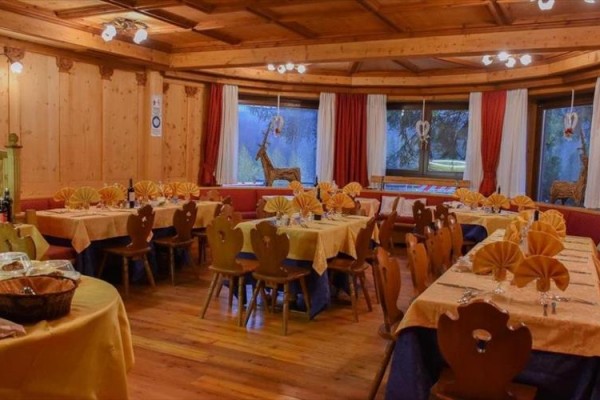 Restauracja z drewnianym wnętrzem, na stołach żółte obrusy i złożone serwetki w kształcie wachlarzy.