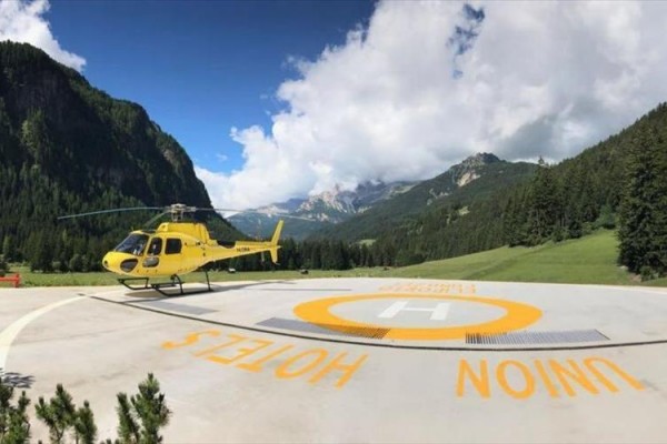 Żółty helikopter na lądowisku otoczony górskim krajobrazem.