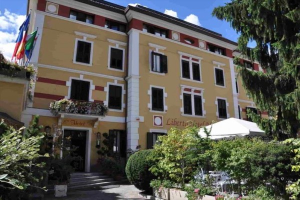 Budynek hotelu z żółtą fasadą i kwitnącym ogrodem z przodu.