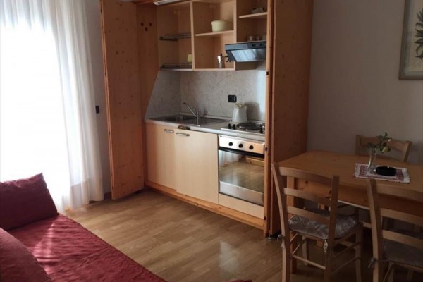 Mały aneks kuchenny z drewnianymi szafkami obok stołu jadalnego i kanapy.