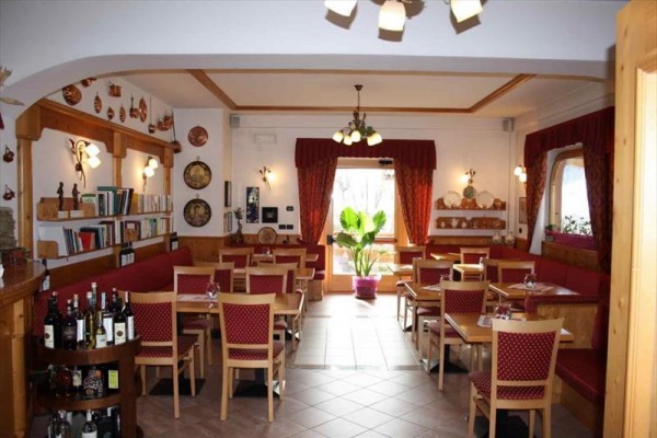 Wnętrze restauracji z drewnianymi meblami, książkami na półkach i dużą rośliną pośrodku.