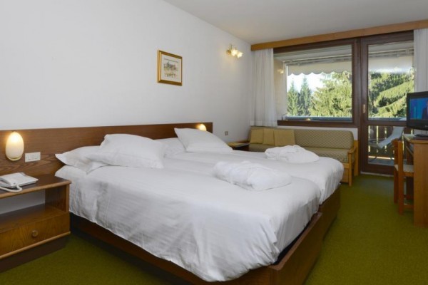 Pokój hotelowy z dużym łóżkiem, kanapą, telewizorem i widokiem na las.