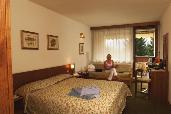 Pokój hotelowy z łóżkiem małżeńskim i kobietą siedzącą na kanapie przy oknie.