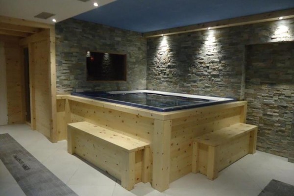Jacuzzi otoczone drewnianymi ławkami w pomieszczeniu z kamiennymi ścianami.