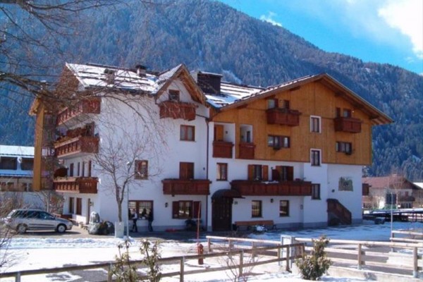 Dwupiętrowy górski hotel z drewnianymi balkonami na tle ośnieżonego zalesionego wzgórza.