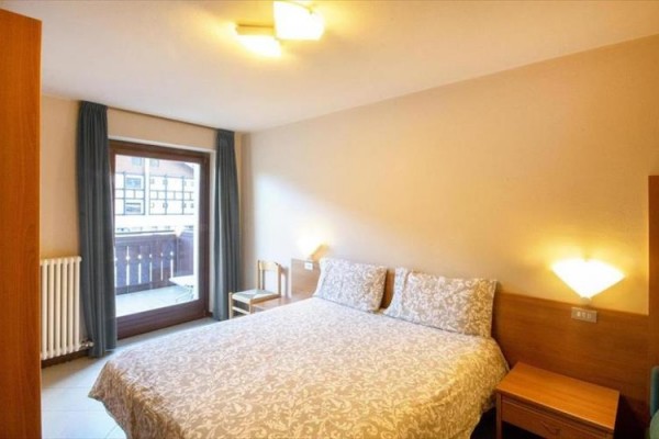 Jasny pokój hotelowy z łóżkiem małżeńskim i balkonem.