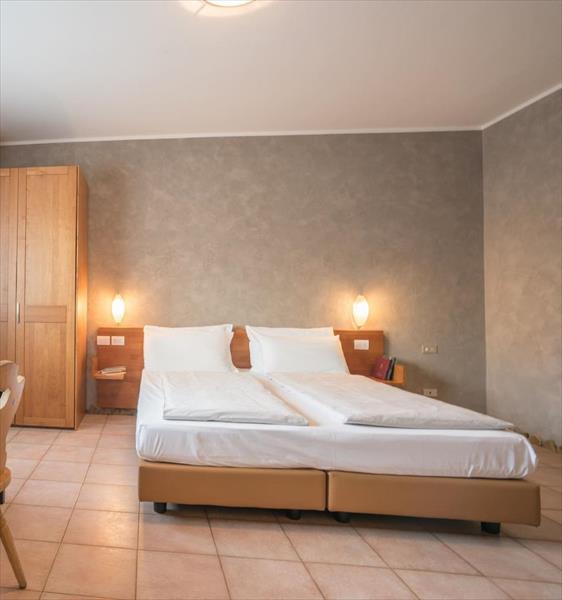Nowoczesny pokój hotelowy z łóżkiem małżeńskim, stolikami nocnymi i drewnianą szafą.