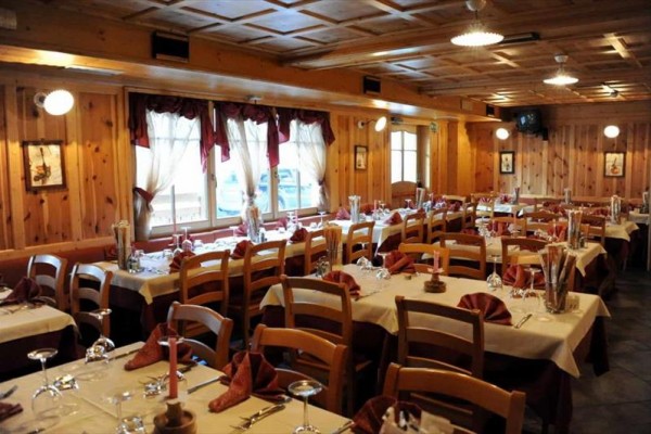 Restauracja z drewnianą boazerią i nakrytymi stołami z białymi obrusami i bordowymi serwetkami.