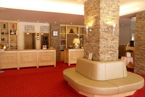 Recepcja hotelowa z czerwonym dywanem, drewnianym blatem i kamiennymi słupami.