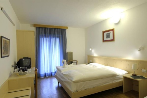 Jasny pokój hotelowy z podwójnym łóżkiem, telewizorem i niebieską zasłoną w oknie.