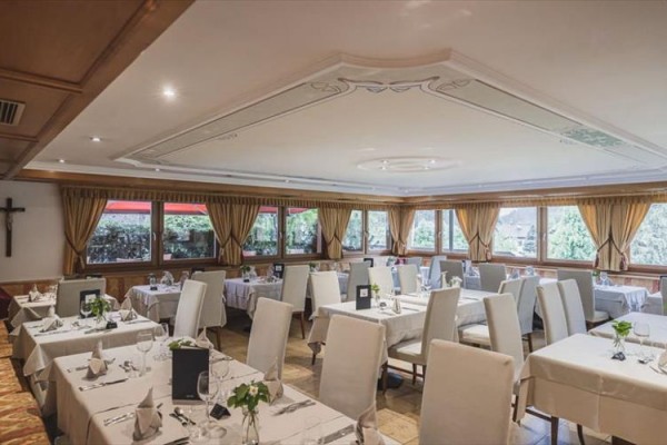 Elegancka restauracja z białymi obrusami i dużymi oknami z widokiem na przyrodę.