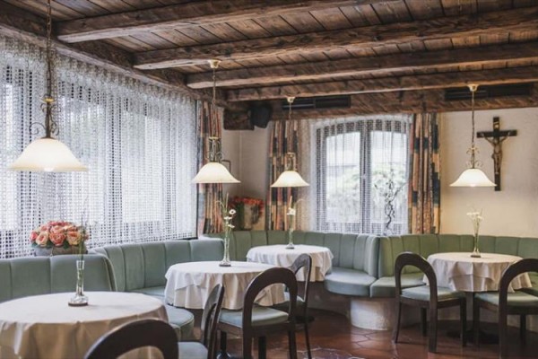 Wnętrze restauracji z drewnianym sufitem i zielonymi kanapami wokół okrągłych stołów.