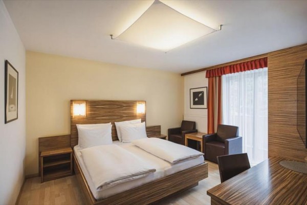 Nowoczesny pokój hotelowy z podwójnym łóżkiem, krzesłami i stołem obok okna z czerwonym zasłoną.