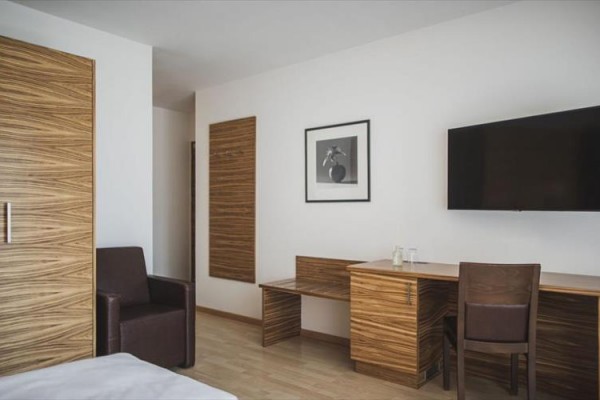 Nowoczesny pokój hotelowy z drewnianymi meblami, telewizorem i artystyczną fotografią na ścianie.