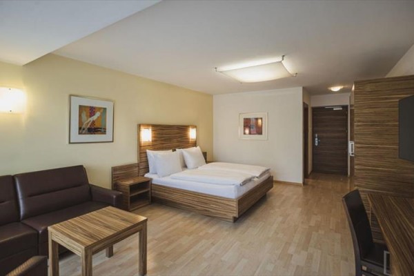 Nowoczesny pokój hotelowy z łóżkiem małżeńskim, sofą i drewnianymi meblami.
