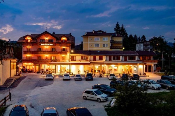 Hotel z oświetloną fasadą i parkingiem pełnym samochodów o zmierzchu.