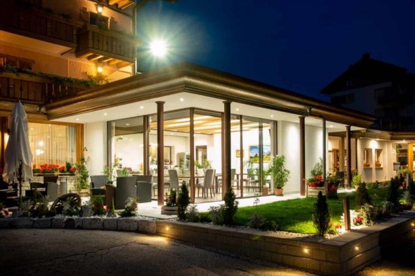 Przeszklona restauracja oświetlona nocą z nowoczesnym wyposażeniem i ozdobami kwiatowymi.